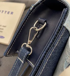 Detailed macro shot of dark denim fabric with white contrast stitching and silver metal buckle