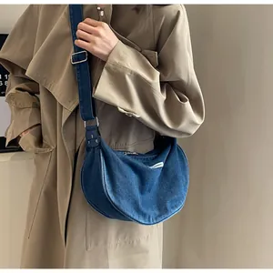 Detail of blue denim crescent bag with adjustable silver buckle strap and white logo label