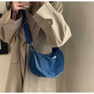 Close-up of a blue denim crescent bag with adjustable strap worn on a khaki trench coat
