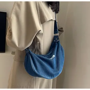 Detail of a dark blue denim crescent bag with a white woven label and metal buckle