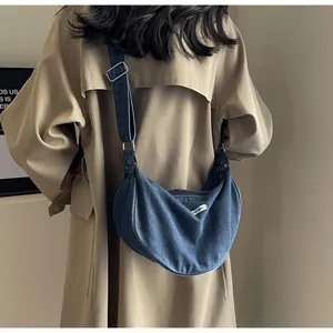 Detail of dark blue denim crescent bag with adjustable wide strap and metal buckle