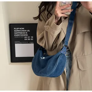 Detailed view of deep blue denim crescent bag worn over a trench coat for casual styling