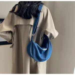 Blue denim crescent moon shoulder bag with wide strap worn with a khaki trench coat