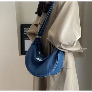 Side view of dark blue denim crescent bag worn with a khaki trench coat for a casual look