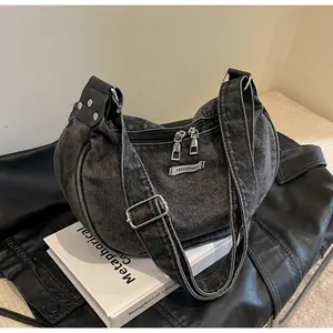 Close-up of washed denim shoulder bag featuring dual zippers and fashion fabric label