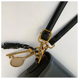 Gros plan détaillé d'un sac en cuir noir avec boucle dorée et pendentif raquette de tennis