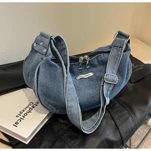 Detail of blue washed denim dumpling bag with adjustable strap and fashion brand label