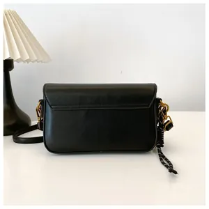 Détail d'un sac bandoulière en cuir noir avec ferrures dorées et accessoire en corde