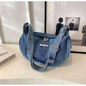 Close-up of blue denim crescent hobo bag with adjustable strap and fashion logo patch
