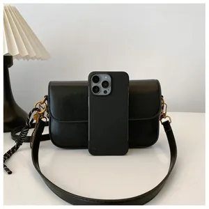 Comparaison de taille détaillée du sac bandoulière en cuir noir avec un iPhone gris