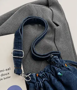 Détail des broderies fleuries et de la bandoulière réglable d'un sac seau en denim