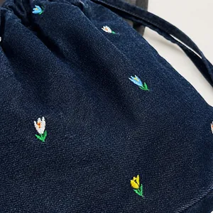 Détail des motifs floraux brodés sur le sac seau en denim bleu foncé à cordon