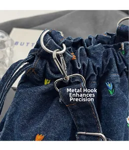 Détail de la broderie florale sur le sac seau en jean bleu marine avec crochets argentés
