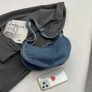 Chic blue washed denim crescent shoulder bag with adjustable strap and silver zipper detail