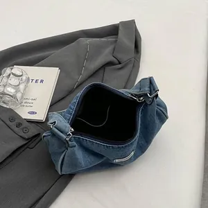 Retro washed denim crescent shoulder bag with fashion label on grey suit background
