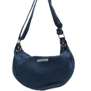 Deep blue denim crescent crossbody bag with wide shoulder strap and metal rivets