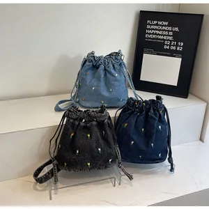 Détail de sacs seaux en denim avec broderie florale et fermeture par cordon de serrage