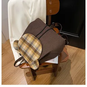 Detail eines braunen Cord-Rucksacks mit karierter Klappe in Bärenform und Kordelzugverschluss