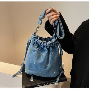 Détail du sac seau en jean bleu clair avec broderies florales et fermeture par cordon