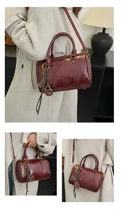 Dettaglio borsa Boston bordeaux in vernice con ciondoli intrecciati e finiture dorate