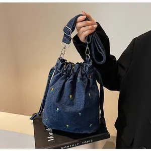 Détail de motifs floraux brodés sur un sac seau en denim bleu avec cordon de serrage