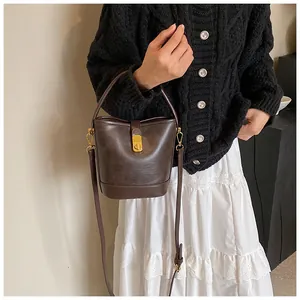 Deep brown leather bucket bag with gold hardware worn by model in a stylish outfit