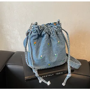 Broderie détaillée de tulipes sur un sac seau en denim bleu clair avec cordon de serrage