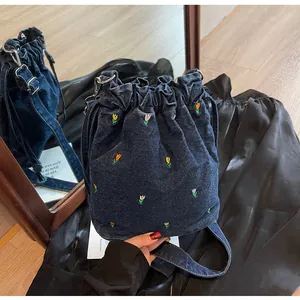 Gros plan du sac seau en denim bleu foncé avec broderies florales et boucle métallique