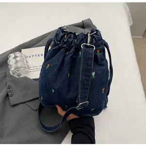 Détail de broderie florale sur sac seau en denim bleu avec cordon et garniture argentée