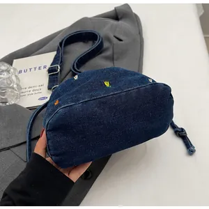 Détail de broderie florale sur sac seau en denim bleu marine avec boucle en métal