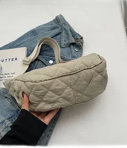 Close-up of beige quilted dumpling bag with adjustable strap on denim jacket