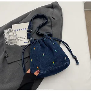 Détail du sac seau en denim brodé de fleurs avec cordon de serrage et bandoulière