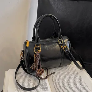 Borsa Boston nera lucida con dettagli dorati e ciondolo vintage su un libro aperto