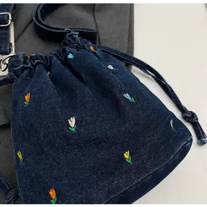 Détail de broderies florales sur sac seau en denim avec bandoulière ajustable