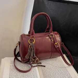 Borsa Boston bordeaux vintage con finiture dorate e tracolla sopra un libro aperto