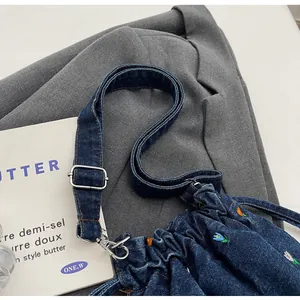 Détail de la broderie florale sur sac seau en denim bleu marine avec bandoulière large