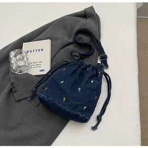 Détail de la broderie florale sur un sac seau en jean bleu foncé avec cordon et boucle métal