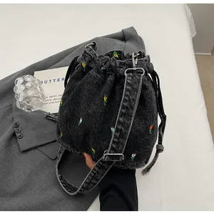 Détail de broderie de tulipe sur sac seau en denim noir avec cordon sur un blazer gris