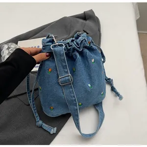 Détail du sac seau en denim avec broderies florales colorées et fermeture à cordon
