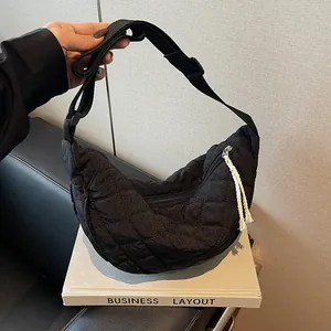 Detailed macro of black quilted crescent bag with adjustable strap on white book prop