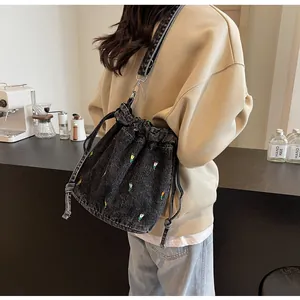 Détail du sac seau en denim noir avec broderies florales colorées et cordon de serrage