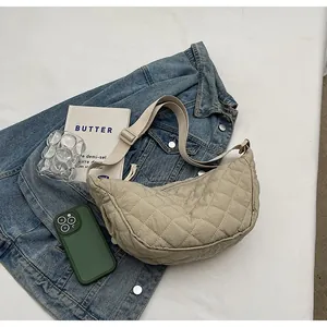 Detail of beige quilted crescent bag with adjustable strap on a denim jacket background