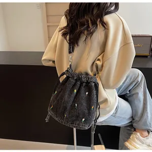 Détail du sac seau en denim noir avec broderie florale colorée et fermeture à cordon