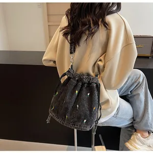 Détail du sac seau en toile noire avec broderie florale porté en bandoulière chic