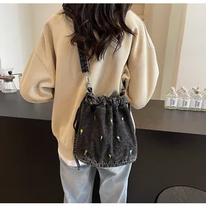 Gros plan détaillé de la broderie florale sur sac seau en denim noir avec cordon