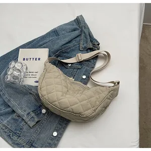 Macro detail of beige quilted crescent bag with adjustable strap on denim background