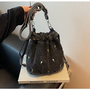 Détail de broderie florale colorée sur un sac seau en denim noir avec cordon de serrage