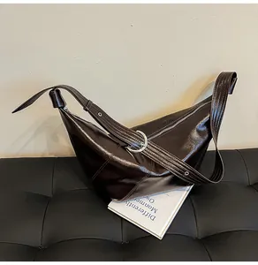 Detail der dunkelbraunen glänzenden Croissant-Tasche auf Lederbank mit Metallschnalle