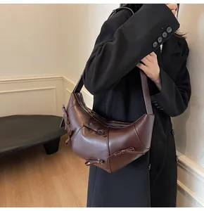 Détail d'un sac demi-lune marron foncé avec nœuds porté sur un blazer noir chic