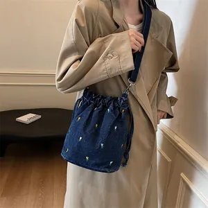 Sac seau en jean bleu marine avec broderie florale porté sur un trench-coat kaki